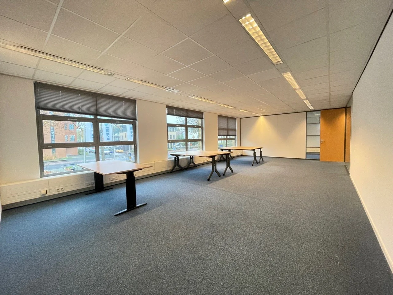 Licht kantoorruimte aan de Rivium 3e Straat met grote ramen, systeemplafond en enkele bureaus.